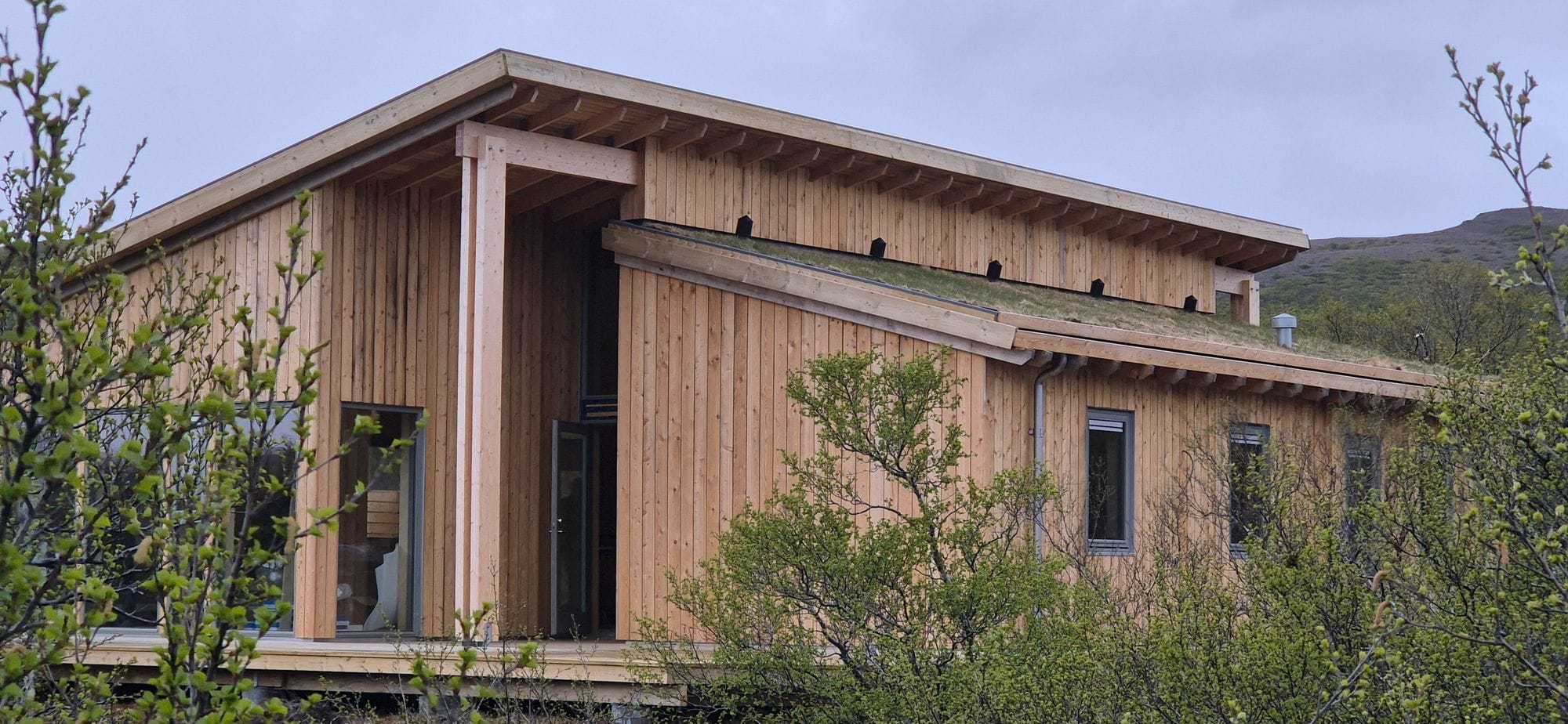 Sumarhús og kjarr í forgrunni.